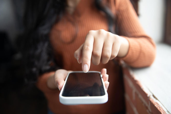 Person using smartphone indoors, illustrating frustration with villainous vacuum cleaner salespeople interaction.