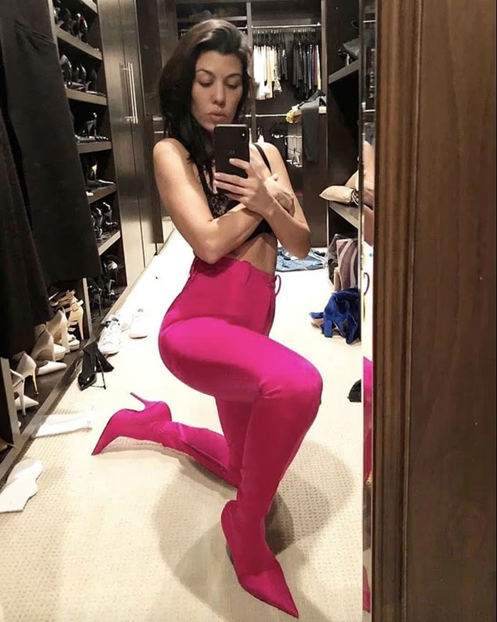 Woman in bright pink boots and pants posing in a messy walk-in closet, capturing a wild video sparking major worry.