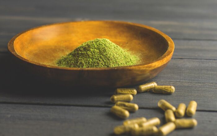 Green herbal powder in a wooden bowl with capsules on a dark wooden surface related to autopsy tech risks. - 14