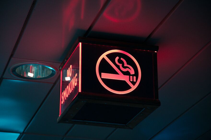 No smoking sign illuminated inside an airplane cabin highlighting in-flight law enforcement and bathroom rules. No smoking sign illuminated inside an airplane cabin highlighting in-flight law enforcement and bathroom rules.