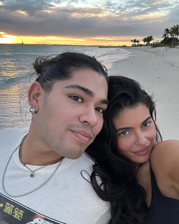 Couple taking a selfie on a beach at sunset, highlighting Kylie Jenner&rsquo;s daughter Stormi in cosmetics ad context.