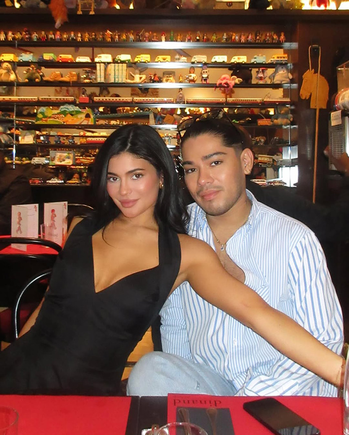 Kylie Jenner posing with a friend in a cozy restaurant, showcasing her beauty and style in a black dress.