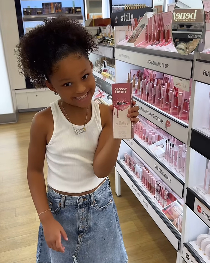 Young girl holding Kylie Cosmetics lip gloss kit while smiling in a makeup store, showcasing the latest cosmetics collection.