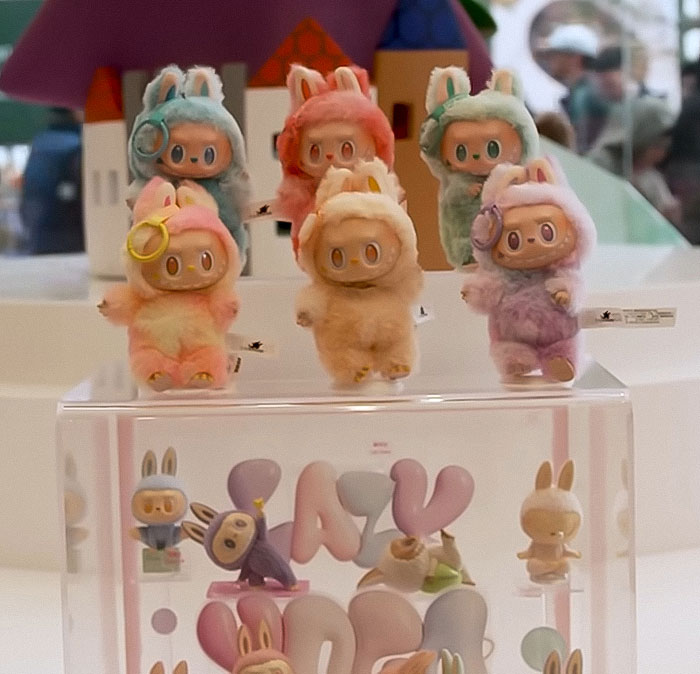Labubu dolls in pastel animal costumes displayed in a collection with a clear glass case beneath them.