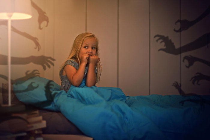 Young girl on bunk bed looking scared as creepy hands&rsquo; shadows appear on bedroom walls at night.
