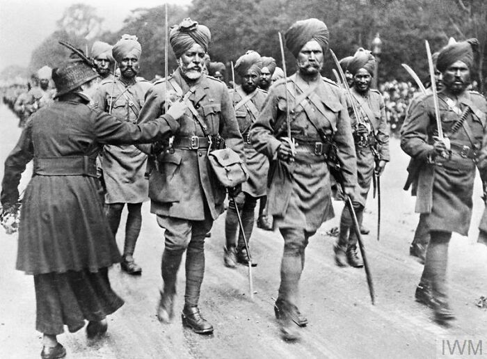 Black and white historical photo of Sikh soldiers in uniform marching during a military parade or inspection.