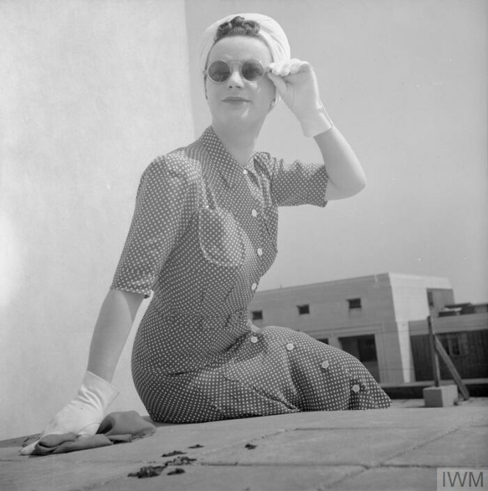 British woman wearing a polka dot dress and sunglasses, showcasing style during WWII restrictions in a black and white photo.