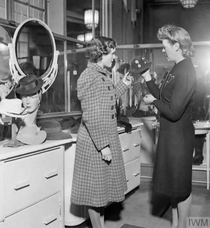 Two British women selecting hats in a shop, showcasing how British women kept their style during WWII restrictions.