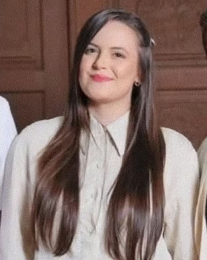 Young law graduate with long dark hair, smiling softly while wearing a beige shirt in an indoor setting.