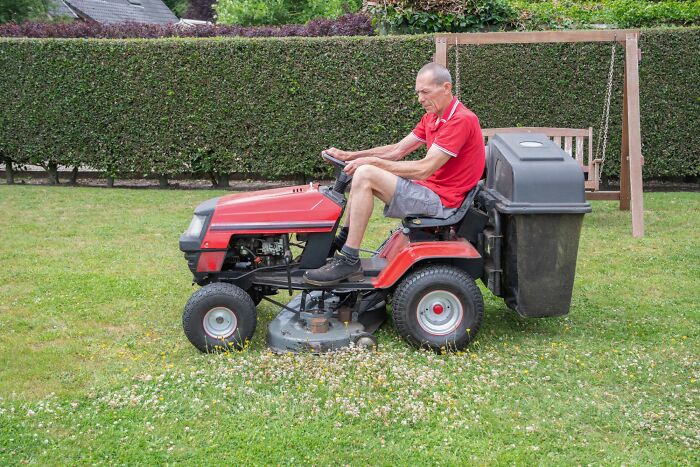 Man in red shirt riding a red lawn mower on grass, illustrating things to avoid to prevent landing on an autopsy tech’s table. - 3