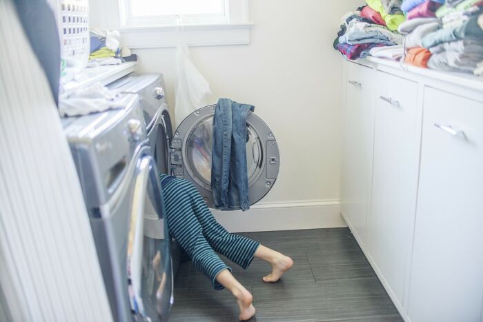 Child with legs sticking out of a washing machine in a laundry room, illustrating risks to avoid for autopsy tech safety. - 4