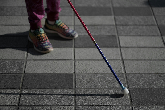 Child wearing colorful shoes walking with a blind cane on a tiled pavement, highlighting kid steals blind cane concept.