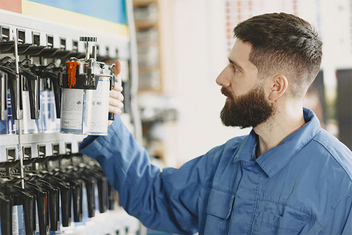 Man in blue coveralls selecting a paint can from a shelf in a workshop, focusing on his task carefully. - 27