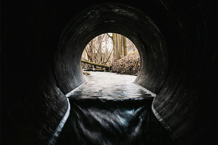 View from inside a dark tunnel with water flowing out toward a wooded area, symbolizing guardian angel protection at Boston Marathon. - 5