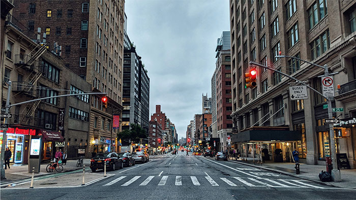 City street scene near the Boston Marathon route with buildings, traffic lights, and pedestrians under a cloudy sky. - 22