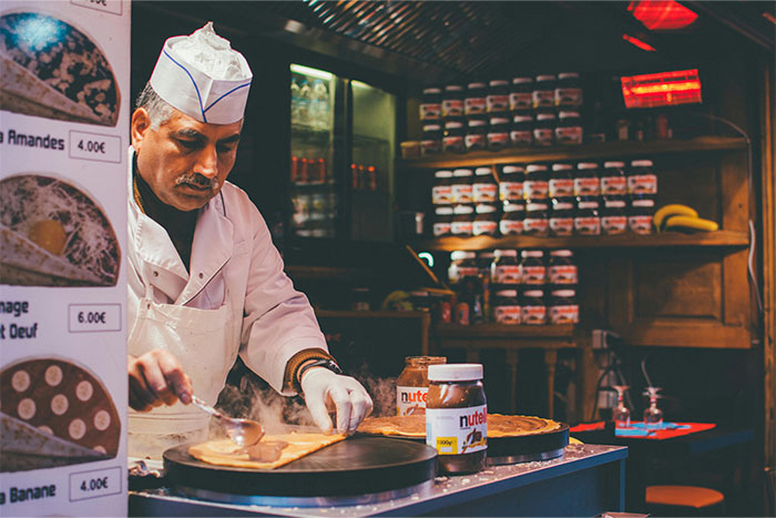 Man preparing crepes in a kitchen, with jars of Nutella nearby, illustrating care and attention at a busy marathon event. - 4