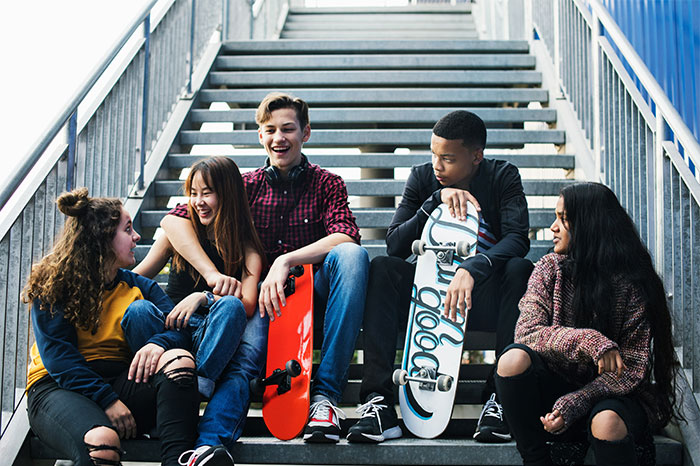 Group of teenagers sitting on stairs with skateboards, enjoying time together near a bright urban setting. - 20