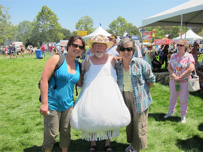 Three people smiling at an outdoor event during the Boston Marathon, enjoying a sunny day with tents in the background. - 33