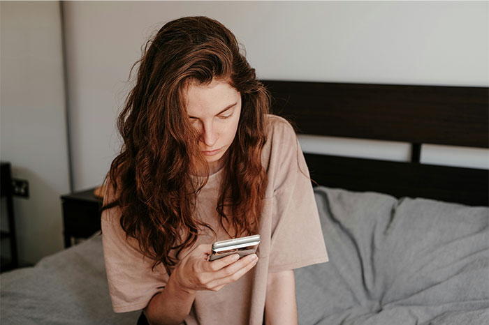 Young woman with long hair sitting on a bed, looking at her phone, reflecting on the Boston Marathon experience. - 36