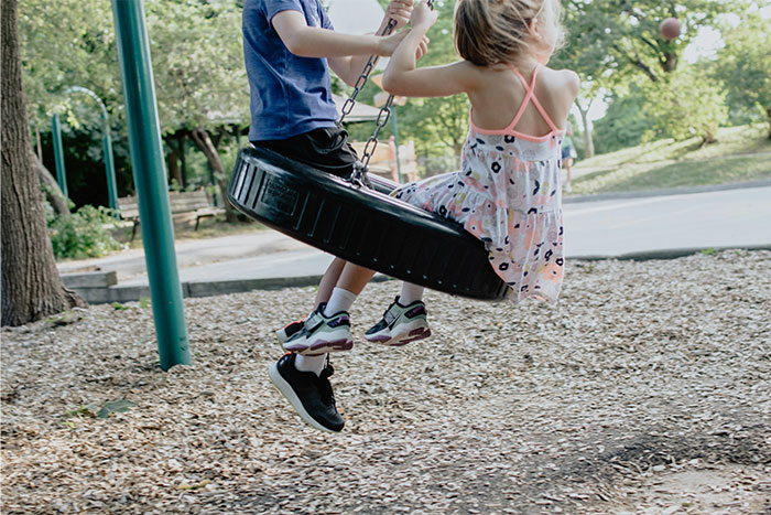 Two children playing together on a tire swing at a sunny park, symbolizing safety and guardian angel protection. - 18