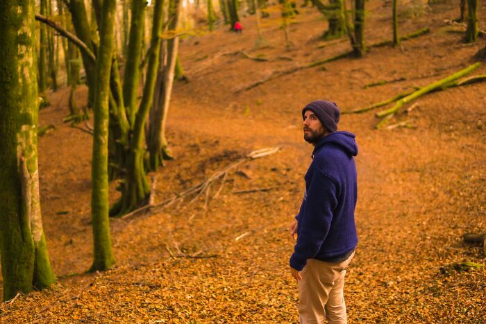 Man in a blue hoodie standing among trees in the woods, evoking the feeling of sleepless nights after time spent outdoors. - 15