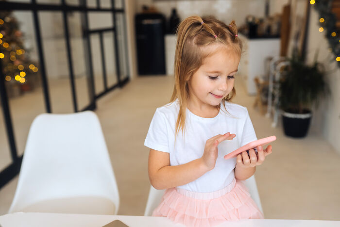Young girl smiling and interacting with an imaginary friend on a smartphone in a bright, modern home setting.