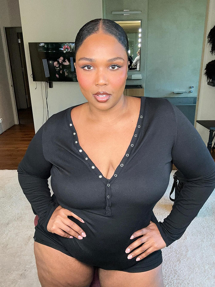 Lizzo posing confidently indoors wearing a black long sleeve outfit with a serious expression and slicked-back hair. - 8