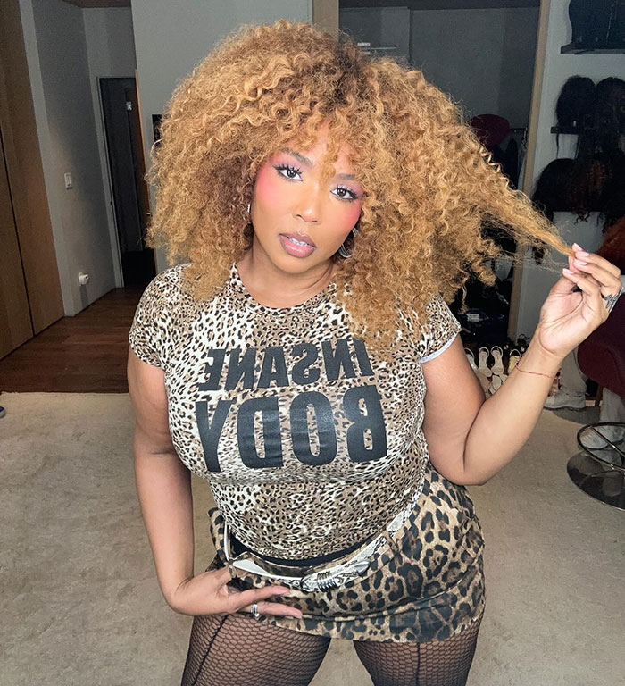 Lizzo in leopard print outfit, posing indoors with voluminous curly hair, referencing Sydney Sweeney ad controversy parody. - 1