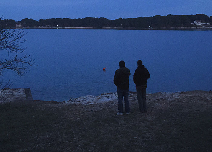 Two people standing by a lake at dusk, evoking a mood fitting for truck drivers sharing terrifying road encounters.
