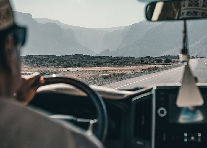 Truck driver wearing sunglasses behind the wheel on a remote highway with mountains in the distance, illustrating road encounters.