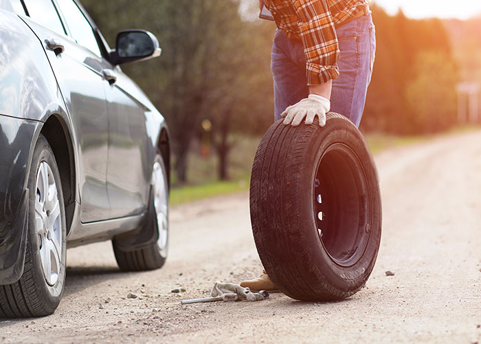 Truck driver changing a flat tire on a rural road during a roadside encounter at sunset.