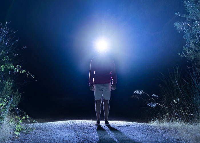 Person wearing a headlamp standing on a dark road at night, illustrating terrifying road encounters of truck drivers.