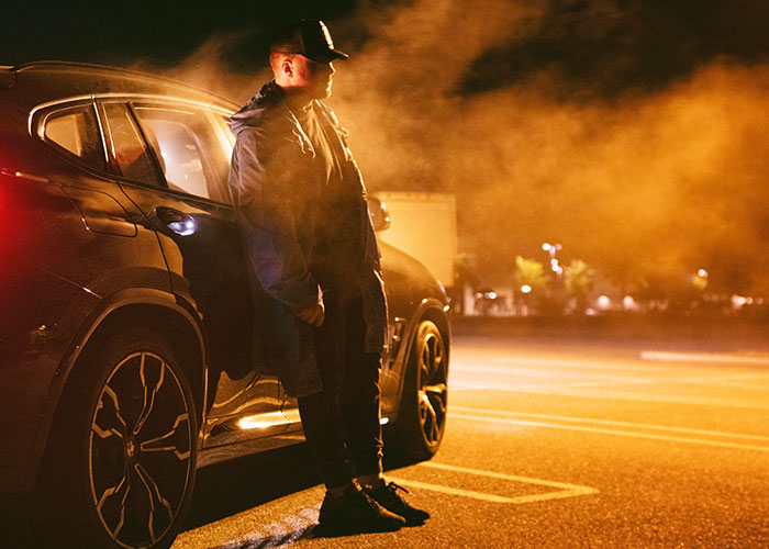 A truck driver stands beside his vehicle at night, surrounded by fog, reflecting on terrifying road encounters.