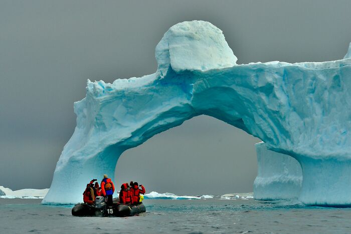 Tourists in red jackets on a boat exploring a large natural ice arch, showcasing fascinating new facts about nature.