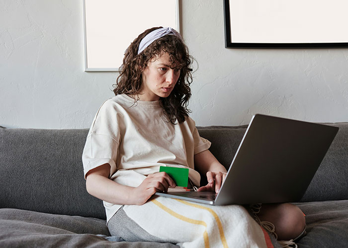 Young woman focused on her laptop while sitting on a couch, discovering loopholes to use effectively from online sources.
