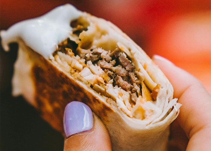 Close-up of a hand holding a burrito, illustrating creative loopholes with food packaging and accidental discoveries.