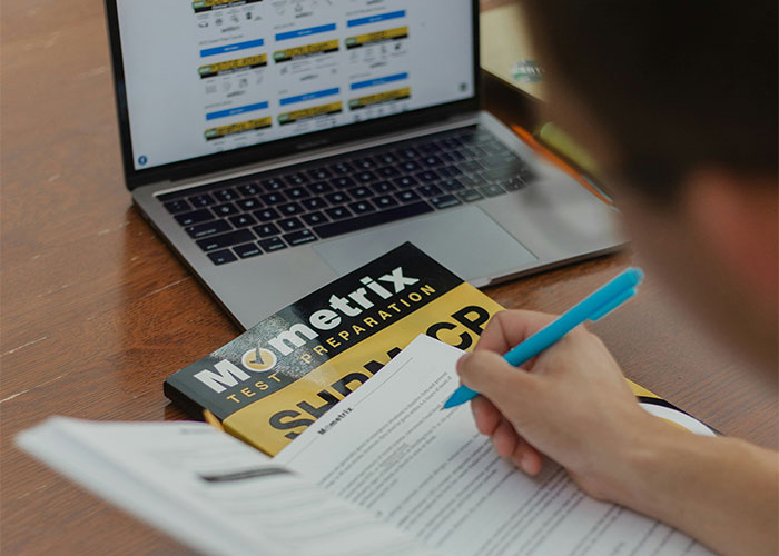 Person holding a pen and writing on paper with a test preparation book and laptop, illustrating loopholes discovery.