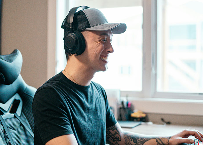 Young man wearing headphones and a cap, smiling while using a computer, illustrating discovering loopholes.