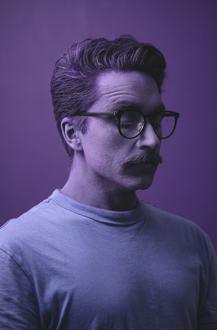 Man with glasses and mustache in purple lighting, reflecting on creepy and terrifying experiences with kids imaginary friends.