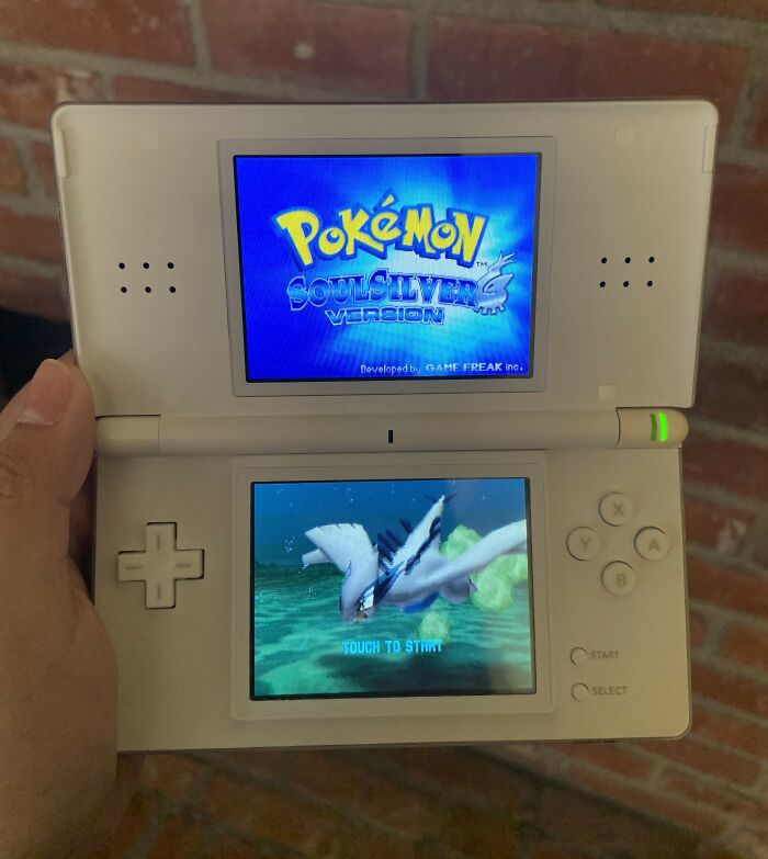 Hand holding an open Nintendo DS gaming console showing Pokemon SoulSilver game, related to shopping and non-substance dependencies.