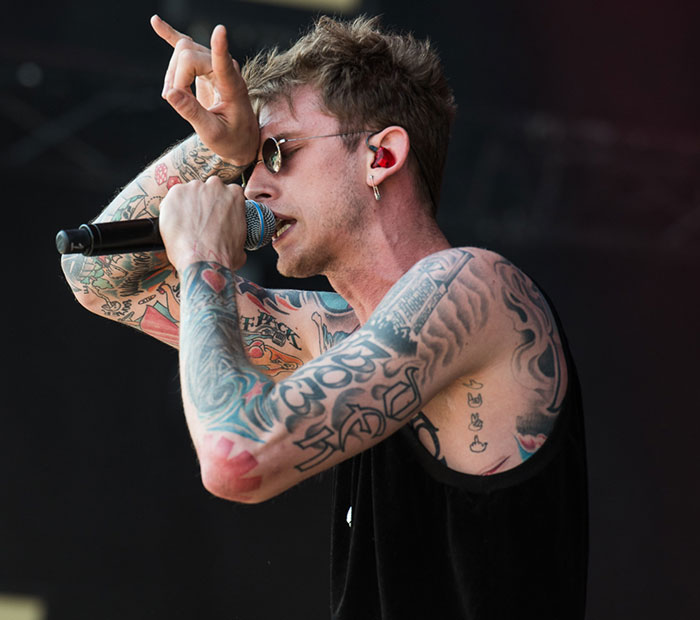 MGK performing on stage, showing tattoos and wearing sunglasses, related to claims of being half alien in interview.