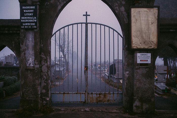 Rusty iron gate with cross at entrance to foggy cemetery, symbolizing widow&rsquo;s legal battle to move back with kids.