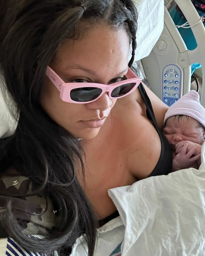 Rihanna holding newborn baby in hospital bed, wearing pink sunglasses, related to maternity dress and bloated cupcake discussion.