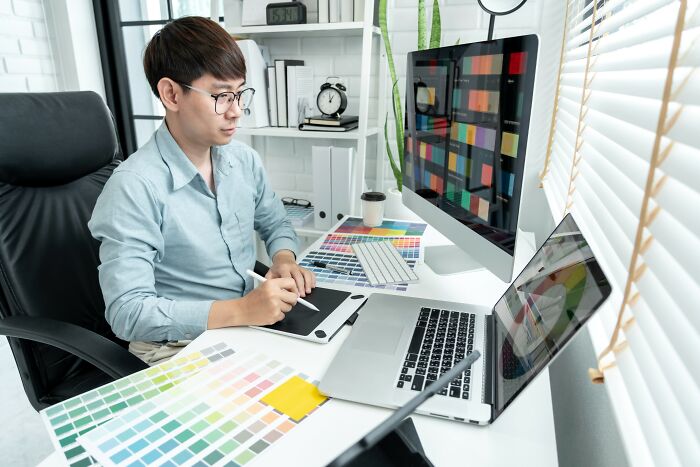 Young man using graphic tablet and laptop, working on colorful designs, representing smartest kids in their class creativity.