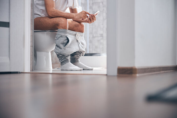 Person sitting on a toilet using a smartphone, illustrating an everyday moment related to cool facts about the human body.