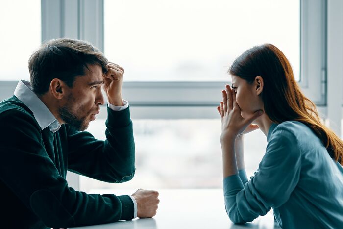 Man and woman sitting at a table in deep conversation, expressing emotions related to love and rejection stories.