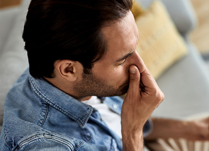 Man in denim jacket pinching nose, reacting to nasty scents flooding home while hosting divorcing friend.