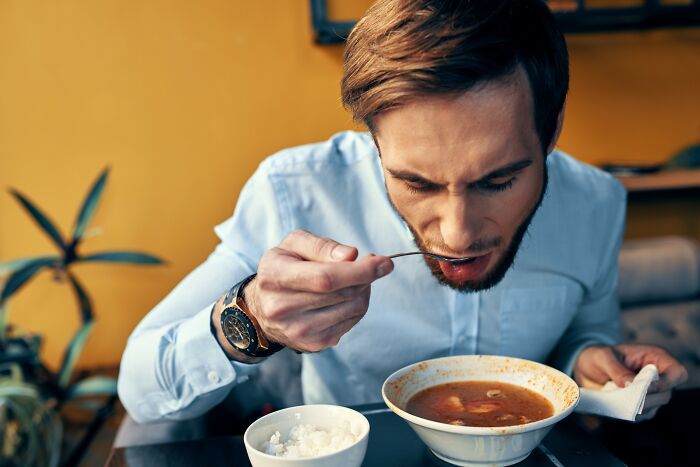 Man in a blue shirt tasting soup while working as a restaurant worker keeping a straight face over orders