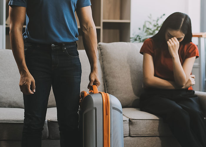 Woman upset on couch after boyfriend told friends she couldn&rsquo;t join couples trip without asking her first.