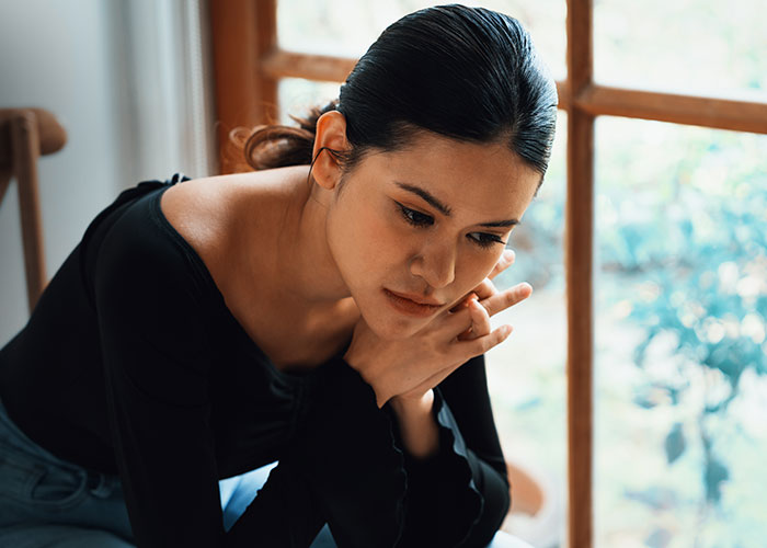 Woman sitting indoors looking thoughtful and upset, reflecting on relationship and trust issues with boyfriend.